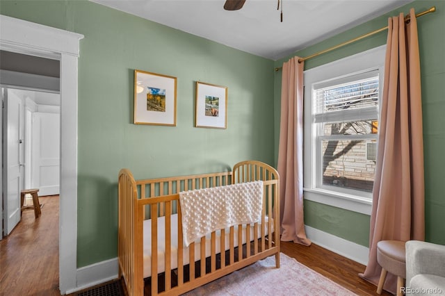 bedroom with a nursery area, hardwood / wood-style floors, and ceiling fan