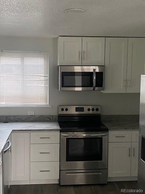 8220 E 104th Way, Henderson, CO 80640 - kitchen with stainless steel appliances, dark wood finished floors, white cabinetry, and a textured ceiling