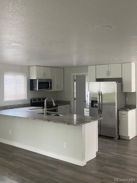 8220 E 104th Way, Henderson, CO 80640 - kitchen with stainless steel appliances, dark wood-style floors, white cabinets, baseboards, and a textured ceiling