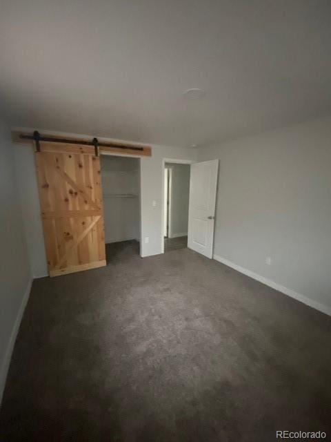 8220 E 104th Way, Henderson, CO 80640 - unfurnished bedroom with a barn door, dark colored carpet, baseboards, and a closet