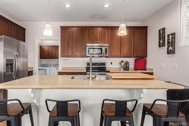 kitchen featuring appliances with stainless steel finishes, hanging light fixtures, washing machine and dryer, and an island with sink