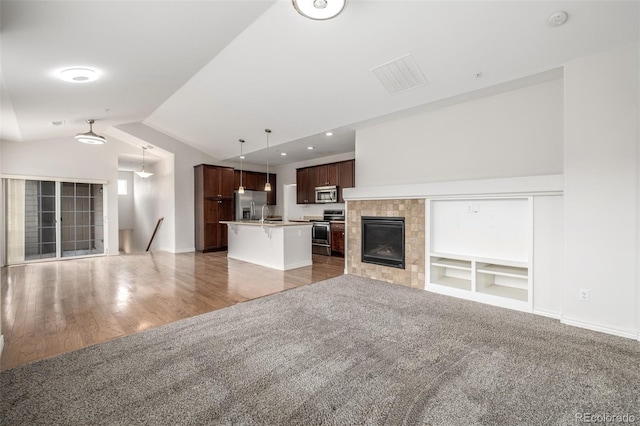 unfurnished living room featuring a tile fireplace, vaulted ceiling, built in shelves, and carpet floors