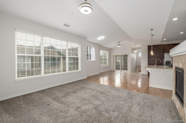 unfurnished living room featuring sink, lofted ceiling, and light hardwood / wood-style flooring