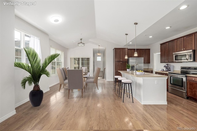 kitchen featuring a center island with sink, light hardwood / wood-style flooring, vaulted ceiling, appliances with stainless steel finishes, and pendant lighting