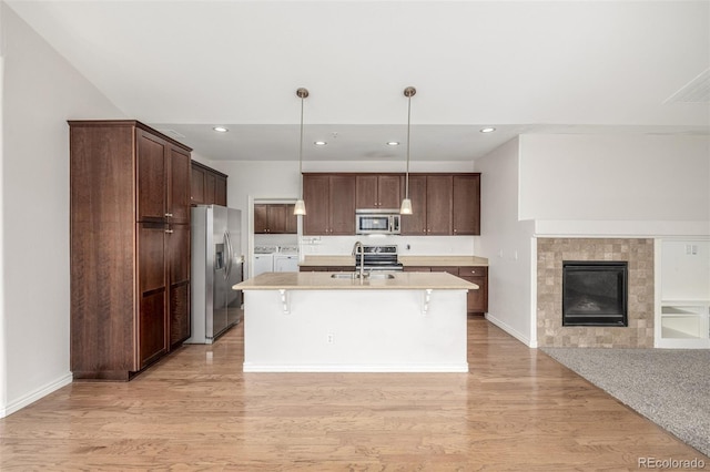 kitchen featuring appliances with stainless steel finishes, a breakfast bar, separate washer and dryer, hanging light fixtures, and an island with sink