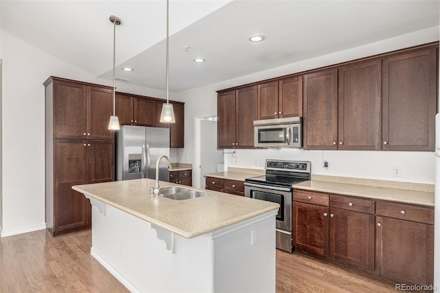 kitchen featuring an island with sink, hanging light fixtures, stainless steel appliances, light hardwood / wood-style flooring, and sink