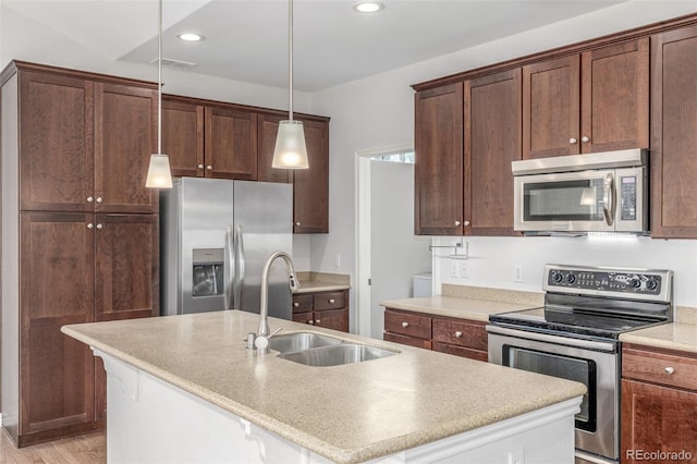 kitchen with a breakfast bar, sink, stainless steel appliances, hanging light fixtures, and a kitchen island with sink