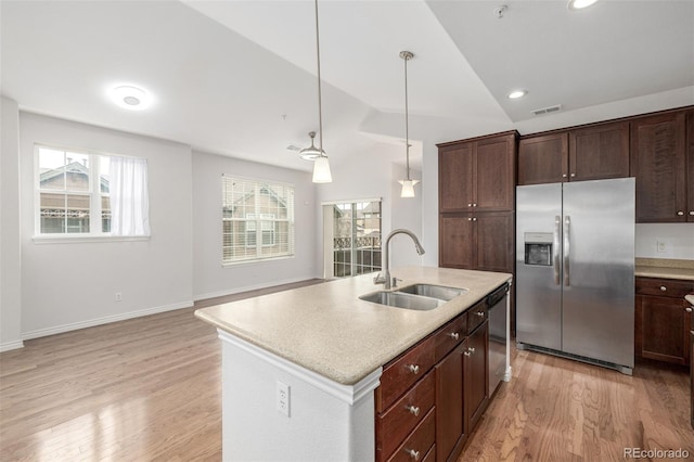 kitchen featuring a kitchen island with sink, stainless steel appliances, decorative light fixtures, sink, and vaulted ceiling