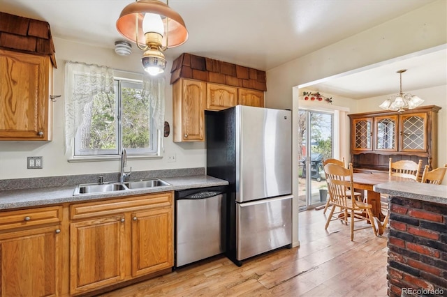 kitchen with light wood-style flooring, hanging light fixtures, a sink, brown cabinets, and stainless steel appliances