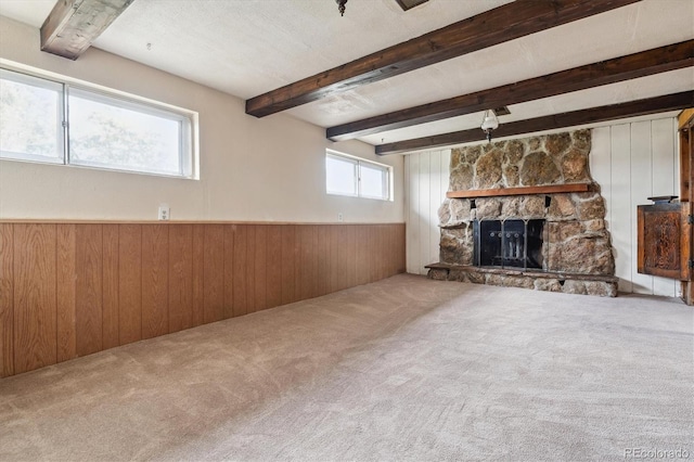unfurnished living room featuring carpet flooring, beam ceiling, a fireplace, wainscoting, and wooden walls