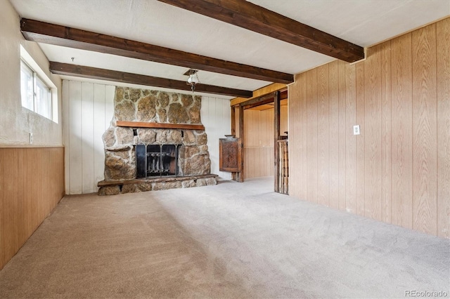 unfurnished living room with carpet flooring, beam ceiling, wood walls, and a stone fireplace