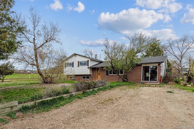 tri-level home featuring dirt driveway and brick siding