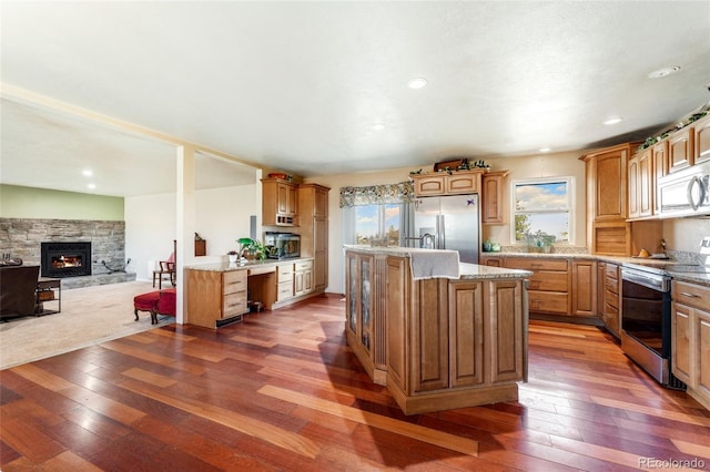 kitchen with hardwood / wood-style flooring, appliances with stainless steel finishes, a stone fireplace, and a kitchen island with sink