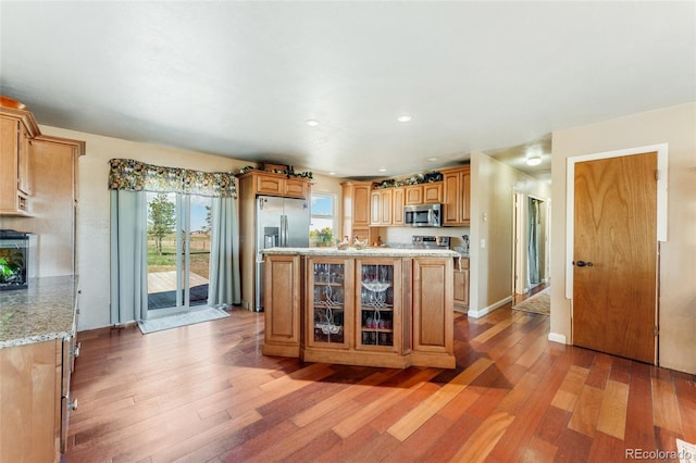 kitchen with glass insert cabinets, light stone counters, stainless steel appliances, and light wood-style floors