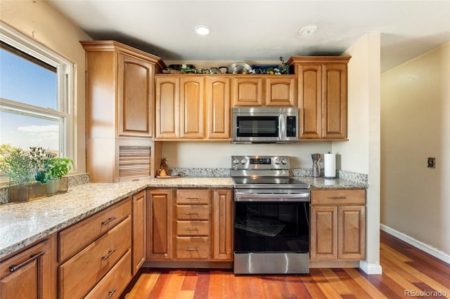kitchen with light stone counters, light wood-style flooring, baseboards, appliances with stainless steel finishes, and recessed lighting