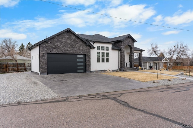 view of front of home featuring stucco siding, driveway, stone siding, fence, and an attached garage