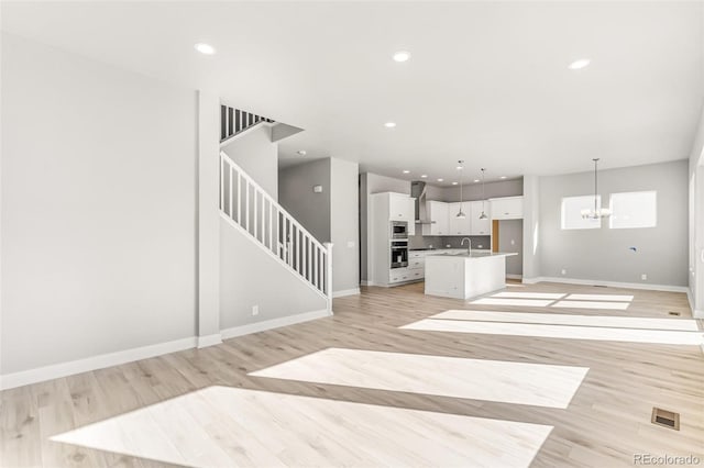 unfurnished living room with an inviting chandelier and light hardwood / wood-style floors