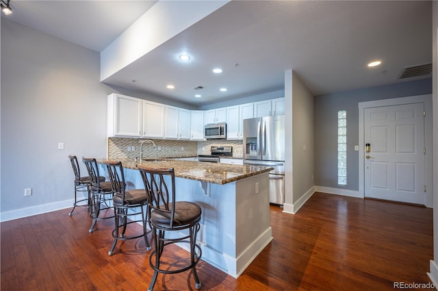 kitchen featuring stainless steel appliances, tasteful backsplash, visible vents, dark stone countertops, and a peninsula