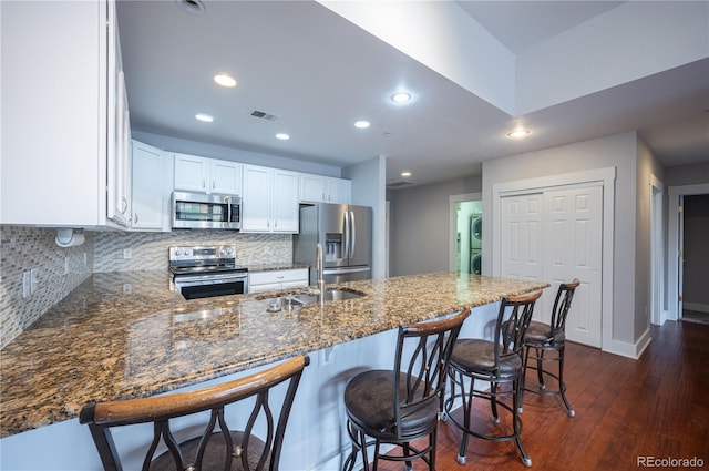 6000 W Floyd Ave Unit 107, Denver, CO 80227 - kitchen with stainless steel appliances, a sink, dark wood-style floors, a peninsula, and dark stone countertops