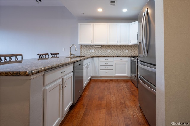 kitchen featuring a peninsula, a sink, visible vents, appliances with stainless steel finishes, and dark stone counters