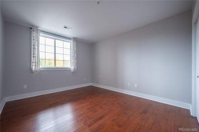 spare room featuring dark wood-type flooring, visible vents, and baseboards