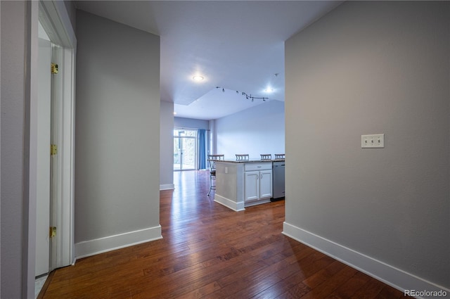 corridor with vaulted ceiling, dark wood-type flooring, and baseboards