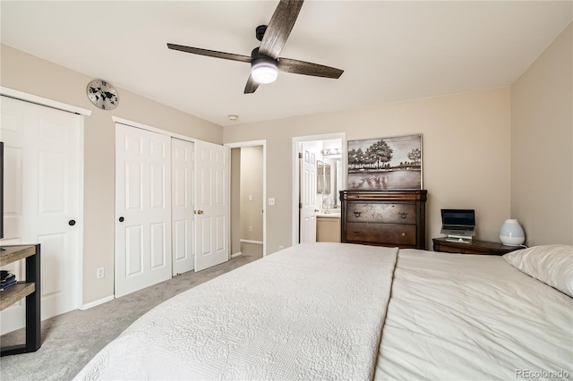 carpeted bedroom featuring ensuite bath, ceiling fan, and two closets