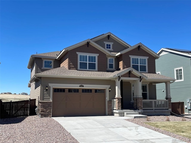 craftsman-style home with a porch, a shingled roof, concrete driveway, fence, and stone siding