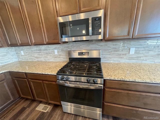 kitchen with appliances with stainless steel finishes, dark wood-style flooring, backsplash, and light stone countertops