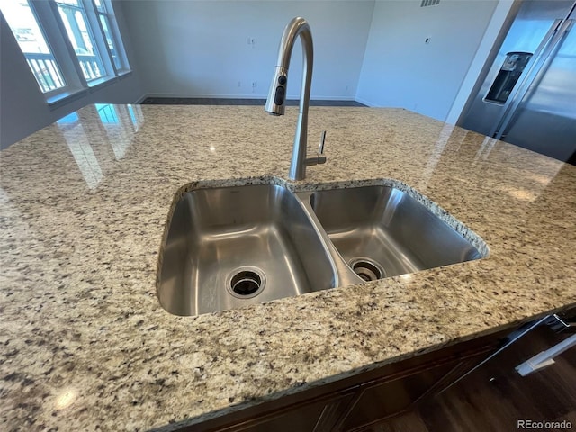 interior details with light stone counters, a sink, and stainless steel refrigerator with ice dispenser