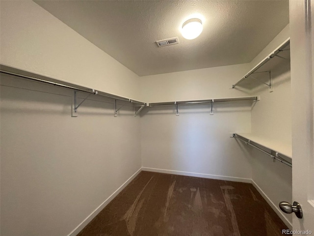 spacious closet featuring dark colored carpet and visible vents