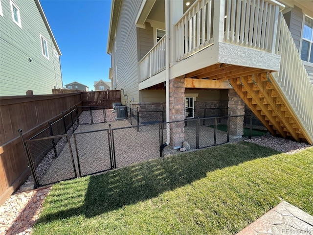 exterior space with stone siding, a fenced backyard, stairs, a yard, and central AC