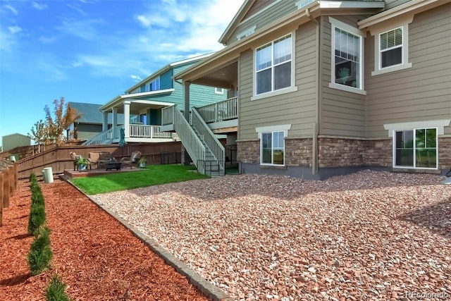 back of property with a patio, an outdoor fire pit, fence, stone siding, and stairs