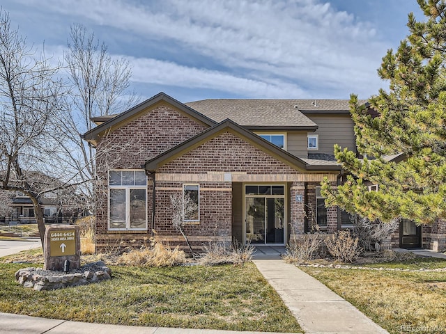 view of front facade featuring brick siding, a shingled roof, and a front lawn