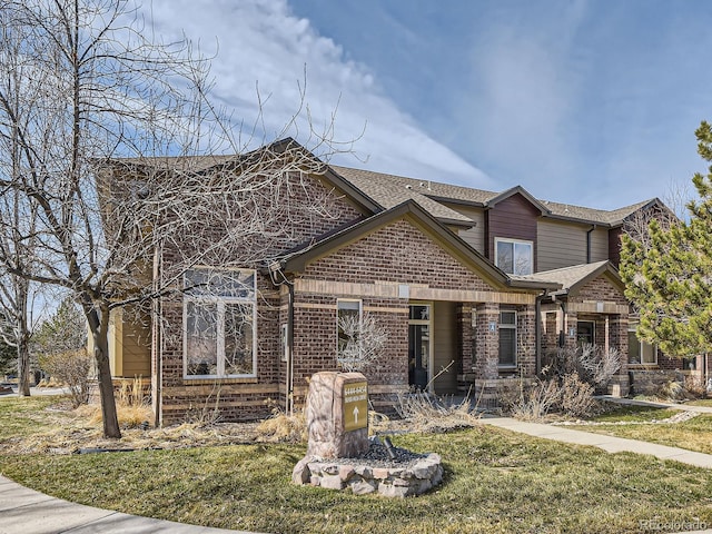 view of front of house with brick siding, roof with shingles, and a front lawn