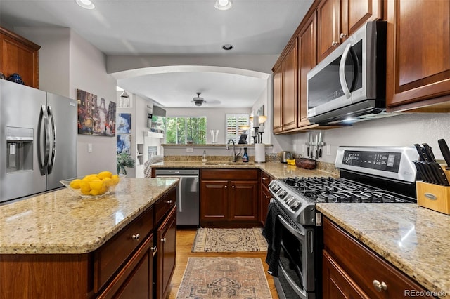 5301 Clovervale Cir, Highlands Ranch, CO 80130 - kitchen featuring appliances with stainless steel finishes, a sink, light stone countertops, light wood finished floors, and arched walkways