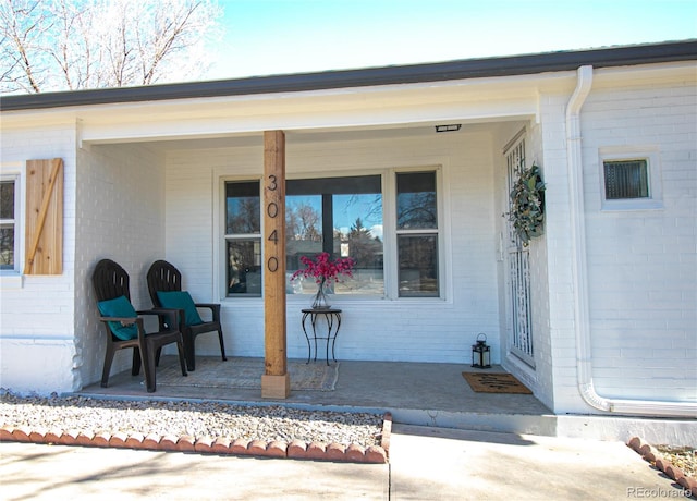 view of exterior entry featuring a porch and brick siding