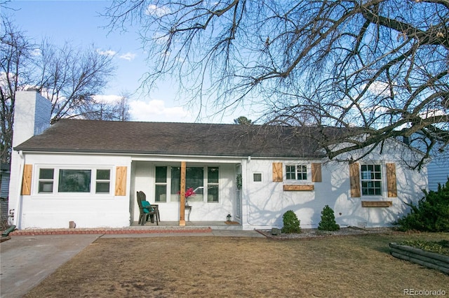 ranch-style home featuring a chimney, roof with shingles, covered porch, a front lawn, and brick siding