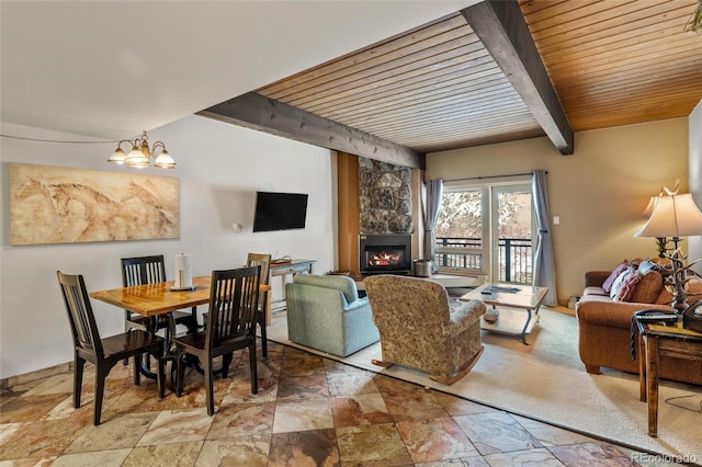 living room featuring beamed ceiling, a stone fireplace, wood ceiling, and a chandelier