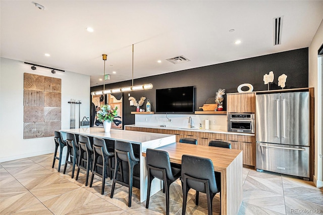 kitchen with a kitchen bar, appliances with stainless steel finishes, kitchen peninsula, decorative light fixtures, and a center island with sink