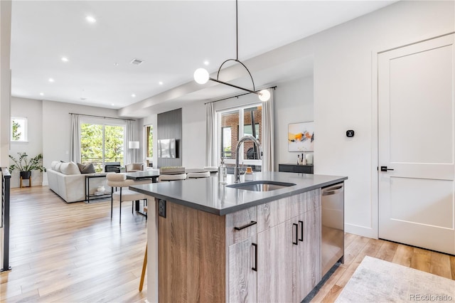 kitchen featuring light hardwood / wood-style floors, stainless steel dishwasher, a kitchen bar, sink, and a kitchen island with sink