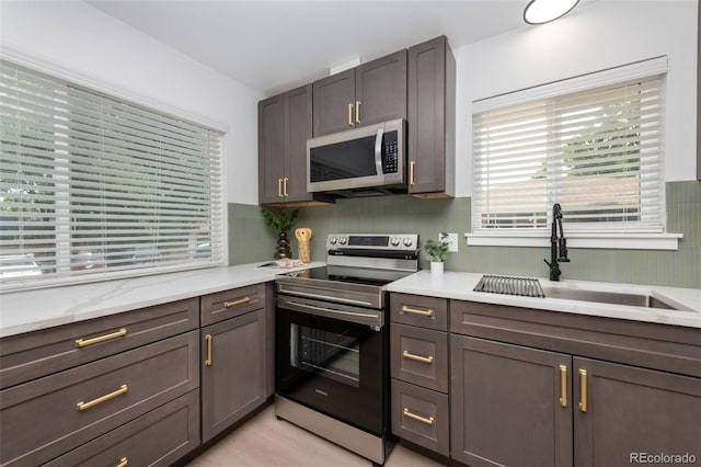 kitchen featuring appliances with stainless steel finishes, sink, light stone counters, light hardwood / wood-style floors, and dark brown cabinetry