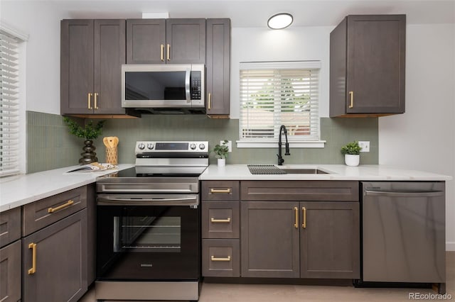 kitchen featuring sink, light stone countertops, dark brown cabinetry, appliances with stainless steel finishes, and backsplash