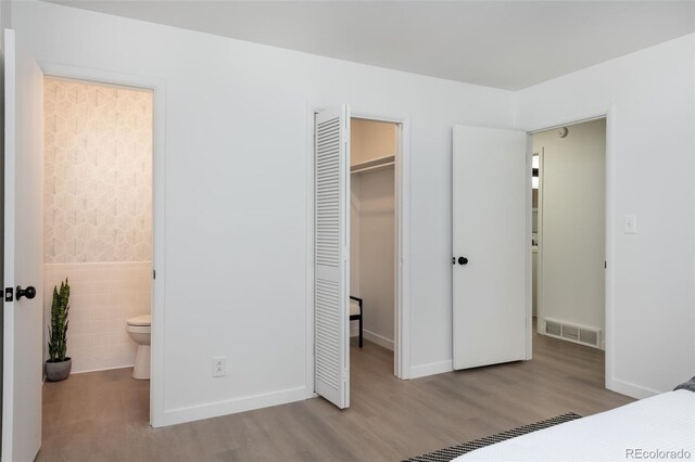 bedroom featuring light hardwood / wood-style flooring, tile walls, ensuite bathroom, a walk in closet, and a closet