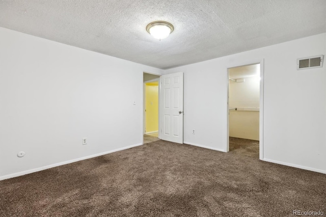 unfurnished bedroom featuring a spacious closet, carpet floors, a textured ceiling, and a closet