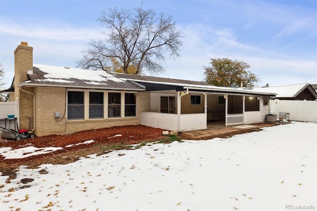 snow covered rear of property with a sunroom