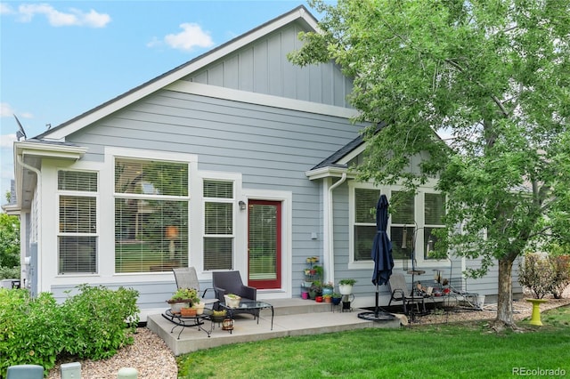 back of house with board and batten siding, a patio area, and a lawn