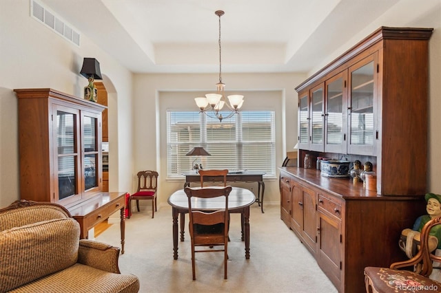 dining space with a tray ceiling, arched walkways, visible vents, an inviting chandelier, and light carpet