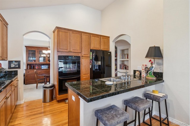 kitchen featuring arched walkways, light wood-style floors, a peninsula, black appliances, and a sink