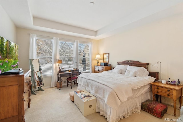 bedroom with a raised ceiling and light colored carpet